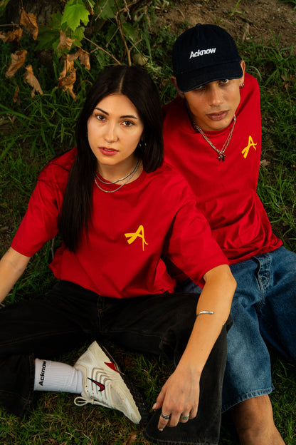 Two models wearing the red Acknow Alfa T-shirt, sitting on grass