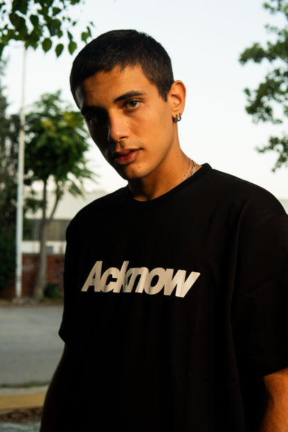 Model wearing the Acknow Classic Logo Tee in black outdoors