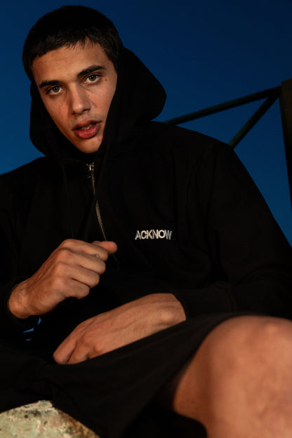 Model wearing the Acknow black zip hoodie with the hood up