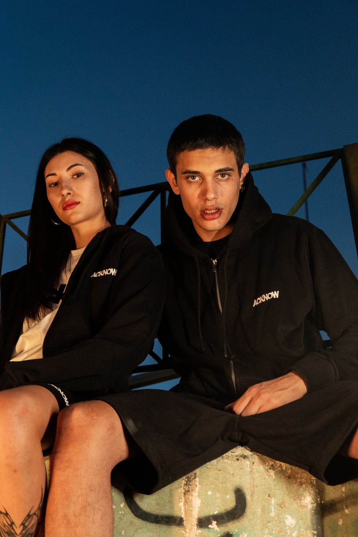 Two models wearing Acknow black zip hoodies